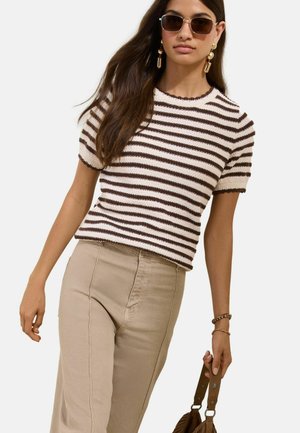 Woman wearing brown and white striped short-sleeve sweater, beige high-waist pants, sunglasses, gold earrings, and holding a brown handbag.