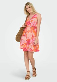 Vestido de verano floral con un diseño de escote en V que presenta tonos de rosa, naranja y melocotón. Una cintura ajustada y una falda acampanada complementan unas sandalias marrones y un bolso de mimbre.