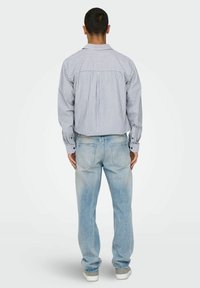 Chemise à rayures bleu et blanc, associée à un jean en denim bleu clair. La chemise a un col et des manches longues.