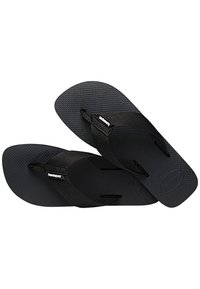 Fekete Havaianas papucsok textúrált, tartós gumitalppal és szövet pántokkal, amelyek mindegyikén logó részletek találhatóak.