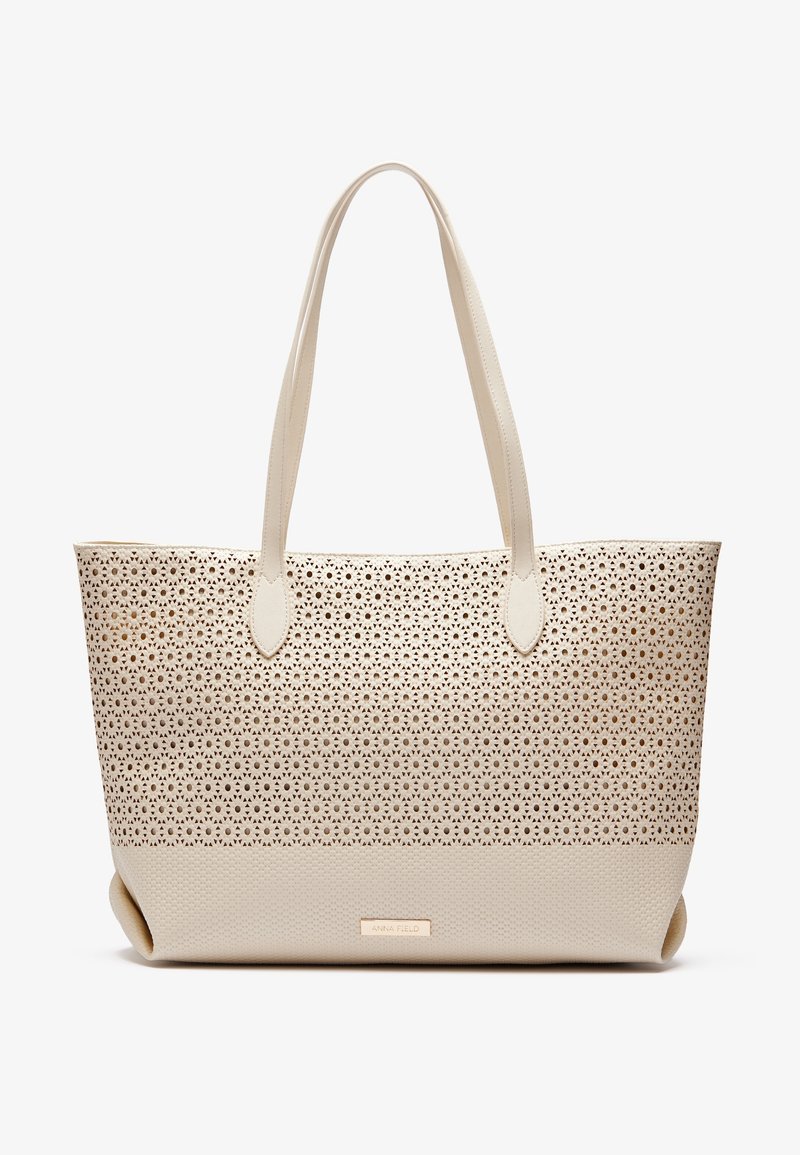 Sac fourre-tout beige avec un motif floral perforé sur la moitié supérieure, base à texture lisse et deux longues anses.