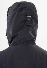 Svart huva jacka med en slät, texturerad tyg, sidofickor med dragkedja och metallbeslag på baksidan av huvan.