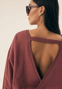 Rdzawoczerwony luźny top z tylnym dekoltem w kształcie litery V, wykonany z teksturowanej tkaniny, z poziomymi paskami na ramionach.