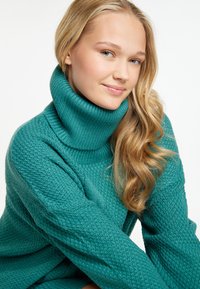 Maglione a collo alto lavorato a maglia in teal, con un motivo testurizzato e colletto a coste. Maniche lunghe con vestibilità rilassata. Finitura in tessuto liscia.