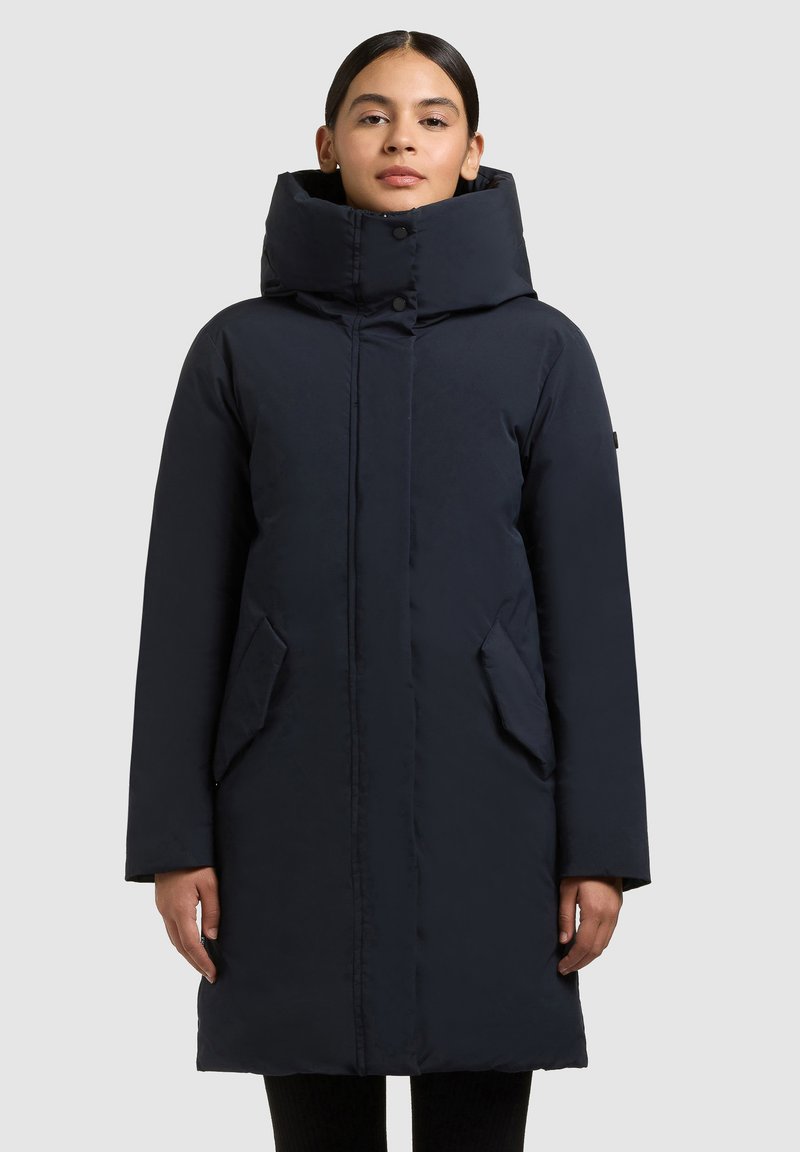 Abrigo largo acolchado azul marino que presenta un cuello alto, botones frontales y bolsillos laterales. Textura lisa e aislante con un diseño de corte recto.