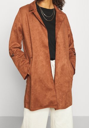 Abrigo de ante marrón con cuello muesca, dos bolsillos laterales y mangas largas con acentos de botones. Lleva puesto sobre una blusa negra.