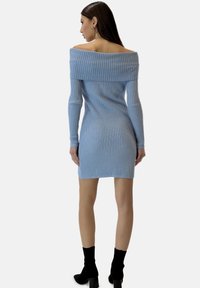 Hellblaues, geripptes Sommerkleid mit schulterfreien Trägern und langen Ärmeln, tailliert geschnitten und mit einem Saum bis zur Mitte des Oberschenkels, kombiniert mit schwarzen Knöchelstiefeln.