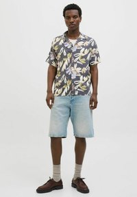 Chemise à manches courtes à motif floral avec une base grise ; shorts de couleur claire ; chaussures marron avec des semelles noires ; chaussettes beiges. Tenue décontractée d'été.