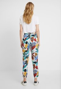 Pantaloni a fantasia con un design di foglie tropicali in colori vivaci, con una vestibilità comoda e polsini elastici, abbinati a una t-shirt bianca.