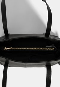 Zwarte leren tote bag met een ruime binnenkant, voorzien van een gouden ritsvak, twee stevige handvatten en een gladde textuur.