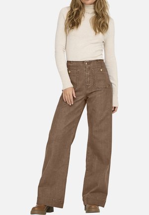 Pantalons larges marron en tissu texturé, avec une taille haute, des poches avant et des coutures contrastées. Associés à un pull léger.