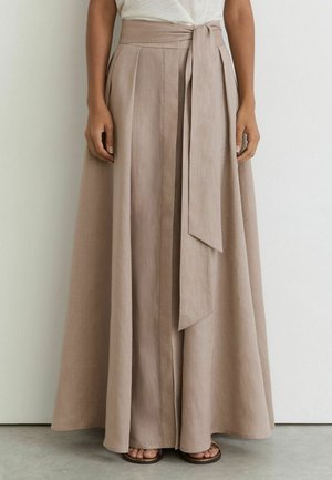 Beige Leinenhose mit weitem Bein, hoher Taille, vorderen Falten und langem gebundenem Gürtel, kombiniert mit braunen Sandalen und einem weißen, in die Hose gesteckten Top.