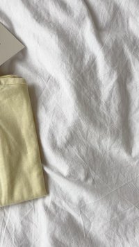 Kahvatu kollane kangas volditud valgele kortsus tekstiilile, ühes ülanurgas on nähtav väike silt, millel on tekstuuriline pind.