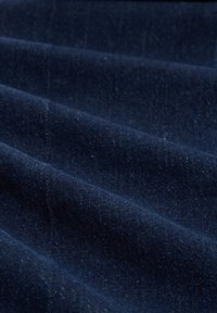 Ciemny denim o widocznej teksturze i subtelnym połysku, złożony w fale, ukazujący bogaty granatowy kolor oraz delikatne różnice w splocie.