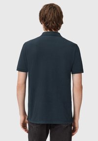 Dunkelblaues Polo-Shirt aus Baumwolle mit einem klassischen Kragen und kurzen Ärmeln. Einfache, einfarbige Textur mit geradem Saum.