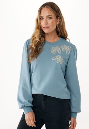 Felpa azzurra con maniche a sbuffo e ricami floreali decorativi in argento e beige. Realizzata in tessuto morbido, con scollo a girocollo.