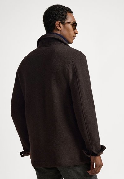 Brūna vilnas maisījuma jaka ar augstu apkakli, ērtu piegriezumu un pogu akcentiem uz aprocēm. Gluda tekstūra un minimālistisks dizains.