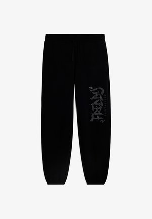 Pantalones jogger negros con cintura elástica y puños ajustados, con los textos "TREND" y "FEEL THE FLOW" en la pierna derecha.