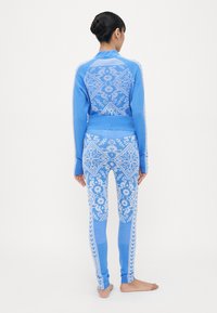 Blå strikket treningssett med blomster mønster; toppen har en glidelås-hals, mens leggingsene har en tettsittende fasong og et sidebranding-detalj.