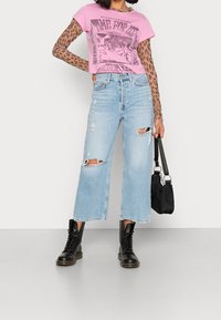 Camiseta corta rosa con estampado gráfico, superpuesta sobre mangas largas con estampado de leopardo. Vaqueros de pierna ancha azul claro con detalles desgastados y botas negras de tobillo.