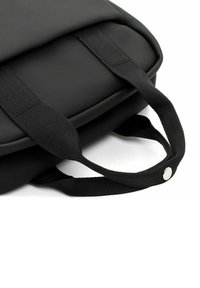 Sac noir avec une finition lisse et mate, doté de deux poignées en tissu robustes et d'un accent en bouton, présentant un design élégant et minimaliste.