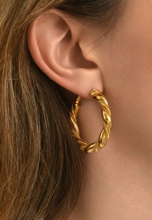 Boucle d'oreille en or avec un design tressé, mettant en avant une finition polie et des accents texturés. Suspendue à un fermoir sécurisé, présentée sur une oreille.