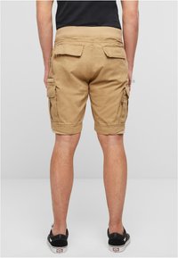 Khaki színű, lazán szabott cargo rövidnadrág, több oldalzsebbel és visszahajtott szegéllyel. Könnyű pamut anyagból készült.