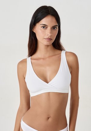 Bralette en coton blanc avec un décolleté en V profond, des bretelles larges et un style enveloppant à l'avant, offrant une apparence lisse et minimaliste.