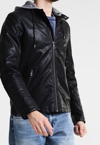 Veste en cuir noir avec une capuche grise, fermeture éclair à l'avant et manches texturées. Dispose de poches latérales et d'une coupe élégante.