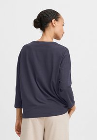 Langärmliges, dunkelblaues T-Shirt mit rundem Halsausschnitt und lockerer Passform. Weicher Stoff mit minimaler Naht und glatter Textur.