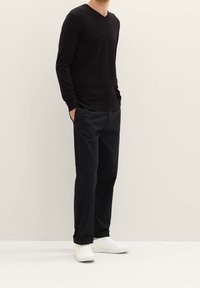 Pull noir à col en V, coupe ajustée, associé à un pantalon noir ample et des baskets blanches. Texture lisse et détails minimalistes.