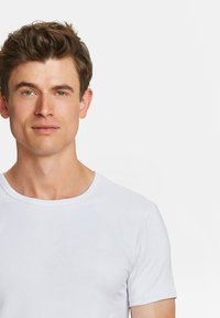 Witte katoenen t-shirt met een ronde halslijn en korte mouwen. Glad textuur met een aansluitend ontwerp, gedragen door een persoon met lichte huid en bruin haar.