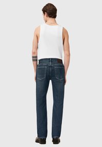Jeans de mezclilla azul oscuro con un corte recto, costuras en contraste y dos bolsillos traseros. Combinados con una blusa sin mangas blanca.