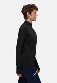 Schwarze, strukturierte Jacke mit hohem Kragen, Reißverschluss vorne und orangefarbenem Reißverschlusszipper. Mit langen Ärmeln und gestreiftem Muster.