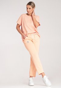 Brzoskwiniowa bawełniana koszulka o luźnym kroju, w zestawieniu z brzoskwiniowymi dresami z wiązaniem w pasie i boczną kieszenią. Całość dopełniają białe trampki.