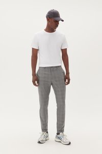 Pantaloni a quadri grigi con una vestibilità slim, abbinati a una t-shirt bianca semplice e un cappellino grigio. Accentuati da scarpe sportive con dettagli blu.