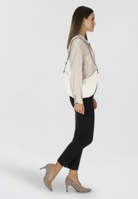 Borsa a spalla bianca in pelle con forma curva, accessori in metallo argentato e tracolla regolabile. Abbinata a pantaloni neri e décolleté beige.