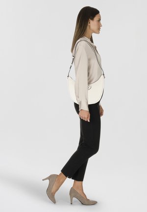 Borsa a spalla bianca in pelle con forma curva, accessori in metallo argentato e tracolla regolabile. Abbinata a pantaloni neri e décolleté beige.
