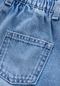 Detail světle modrého denimu s našitým kapsou a pružným pasem.