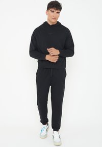 Black hoodie with a front pocket, paired with elastic waist black joggers. Model wears white and gray sneakers with blue accents.