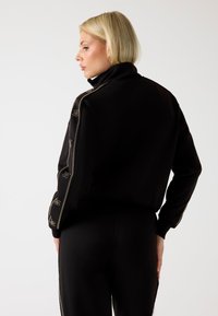 Giacca nera con zip laterale, dettagli ricamati lungo le maniche e colletto alto per un maggiore calore e stile.