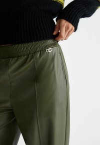 Pantalones de imitación cuero verde oliva con cinturilla elástica, que presentan un cierre decorativo plateado en el lateral para un detalle adicional.