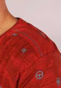 Röd skjorta med subtila racinginspirerade mönster, inklusive ett ratt och rutiga flaggor på en persons axel och övre bröstområde.