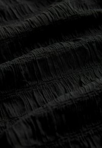 Tejido negro con textura y superficie arrugada, con costuras horizontales que crean una apariencia estratificada. Caída suave y brillo sutil.