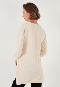 Sudadera de color beige claro con mangas largas, corte relajado, aberturas laterales y puños de canalé. Tejido suave con una textura lisa.