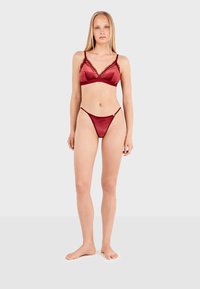 Bralette en satin bourgogne avec bordure en dentelle et fines bretelles, accompagné d'un thong à dos en dentelle assorti. Texture lisse, design minimaliste.
