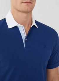 Tmavomodrá polo košeľa s bielym golierom, s gombíkovou légiou a malým logom na hrudi. Vyrobená z texturovanej bavlny.