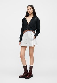 Μαύρο cropped φούτερ με κουκούλα, καφέ τοπ, γκρι ελαστική φούστα με πλευρικές ρίγες και καφέ μπότες μέχρι το γόνατο από δερμάτινο λάστιχο. Απλός σχεδιασμός, casual εμφάνιση.