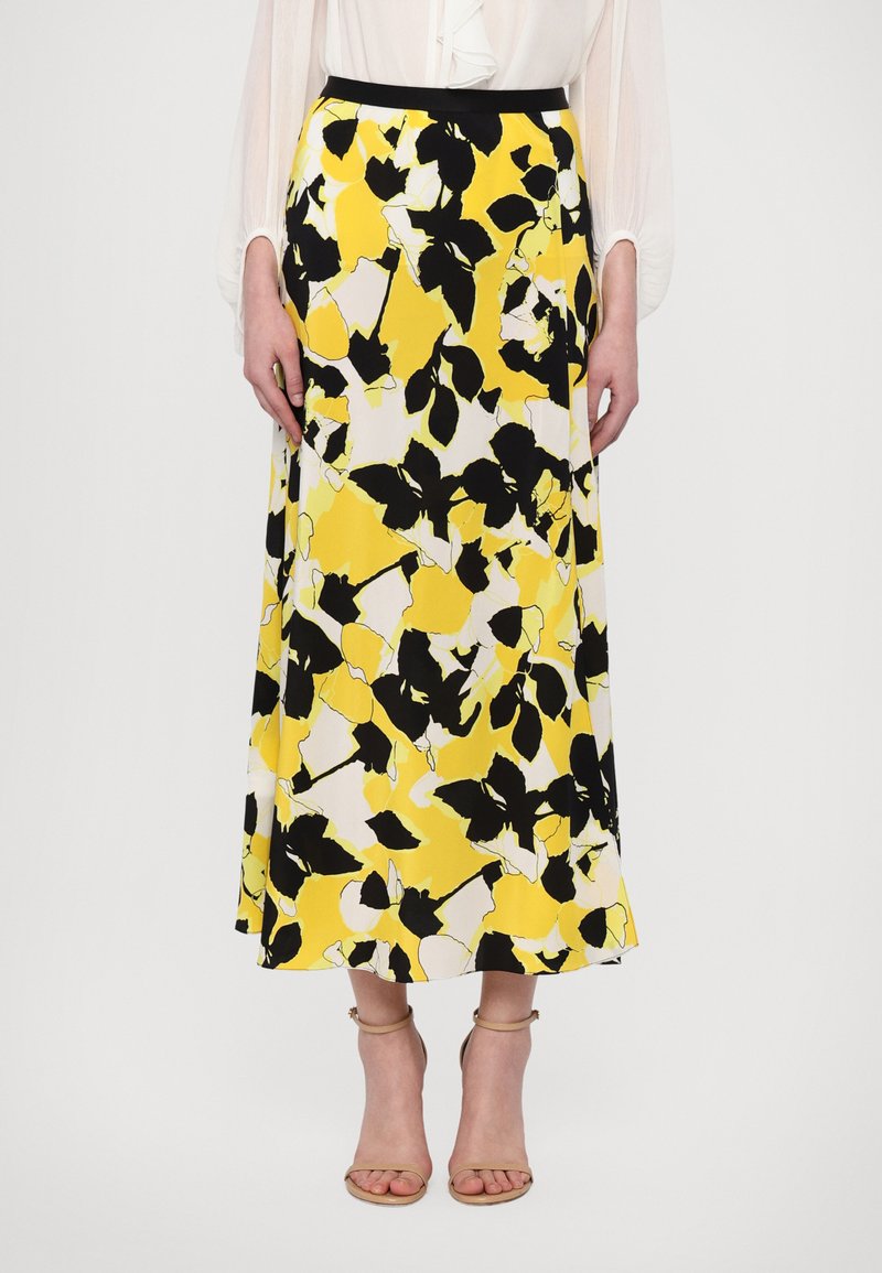 Maxi skirt featuring a floral pattern in yellow, black, and white, with a solid black waistband. Made from lightweight fabric, it has a smooth texture.