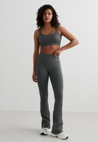 Grijze geribbelde sportcrop top en bijpassende hoge flared leggings, ontworpen voor comfort en flexibiliteit, gecombineerd met witte sneakers.